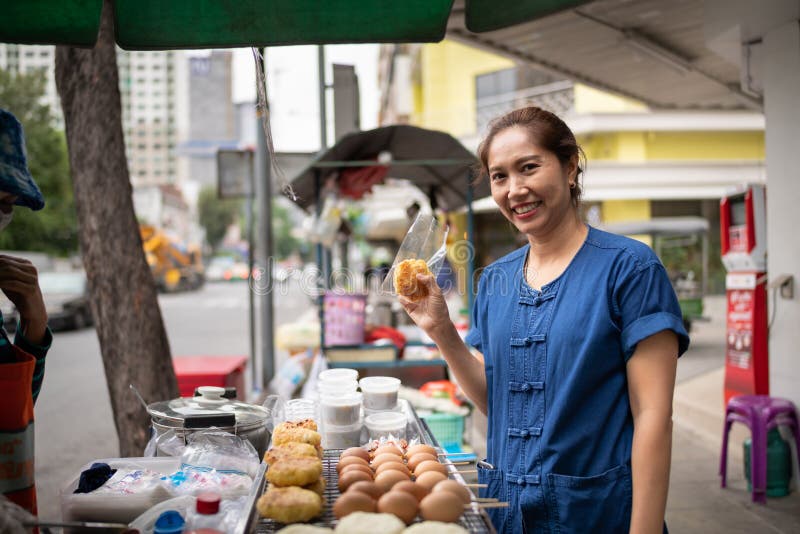 亚裔从一个街道食品厂家的推车的妇女买的午餐在唐人街在曼谷，泰国 库存照片